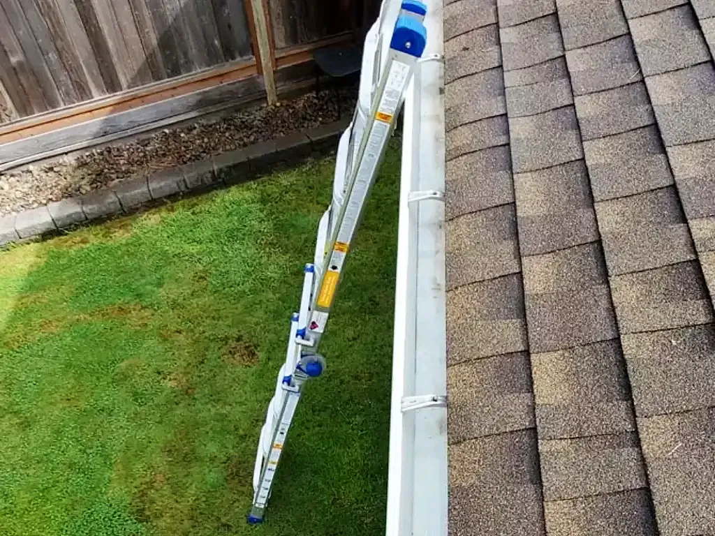 Extension ladder against the gutter of a shingle roof over a lawn