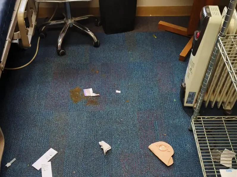 Stained office carpet with scattered debris beside a desk chair and heater