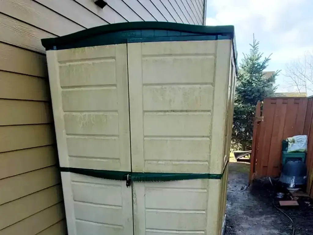 Dirty plastic backyard storage shed against house siding