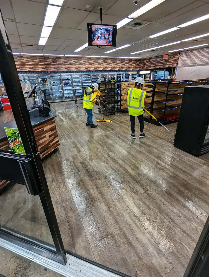 Two Superhero Cleaning crew members in hard hats and hi-vis vests mopping a store sales floor