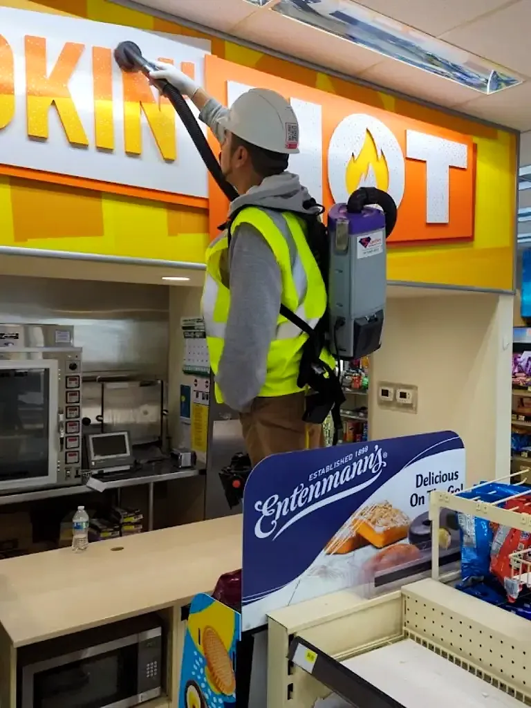 Superhero Cleaning crew member in a hi-vis vest vacuuming the hood above a store hot food counter